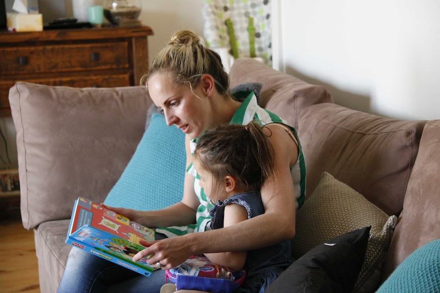 A woman reading a book to a young girl in a living room