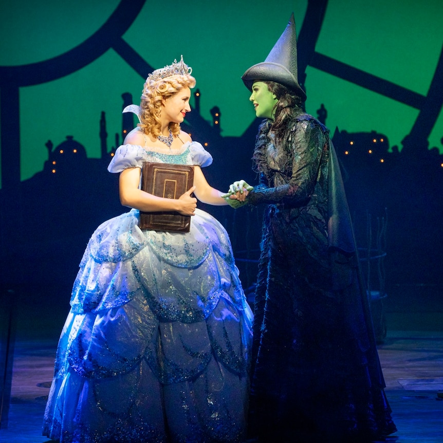 Courtney Monsma and Sheridan Adams as Glinda and Elphaba. Courtney is in a blue gown and Sheridan is in a black witch costume.