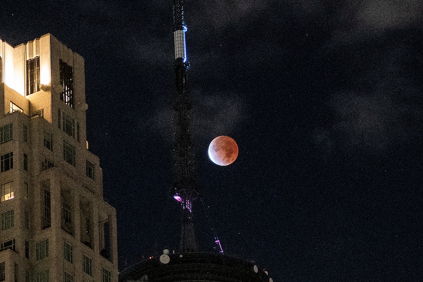 An orange moon in the night sky beside a tall tower 
