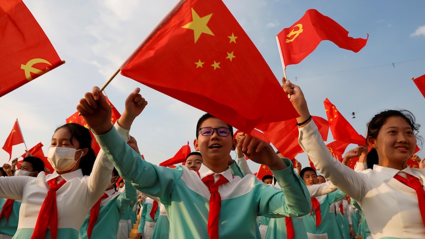 A close up of a large group of performers in blue and white uniforms waving CCP flags at centenary celebrations.  