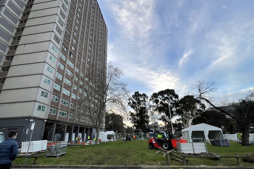 A high-rise apartment against the blue sky with white tent on the grassy park in front.