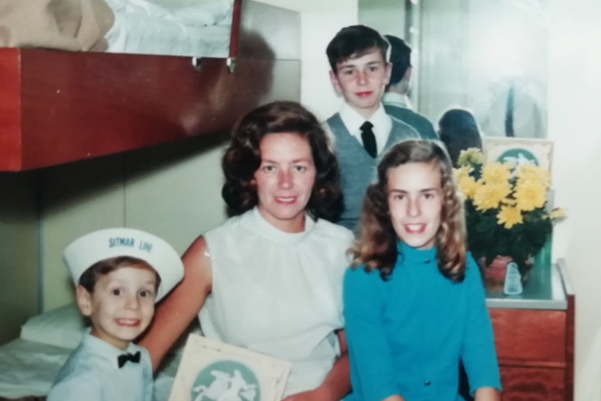 A film photograph shows a mother with her three young children seated around her in a ship cabin.