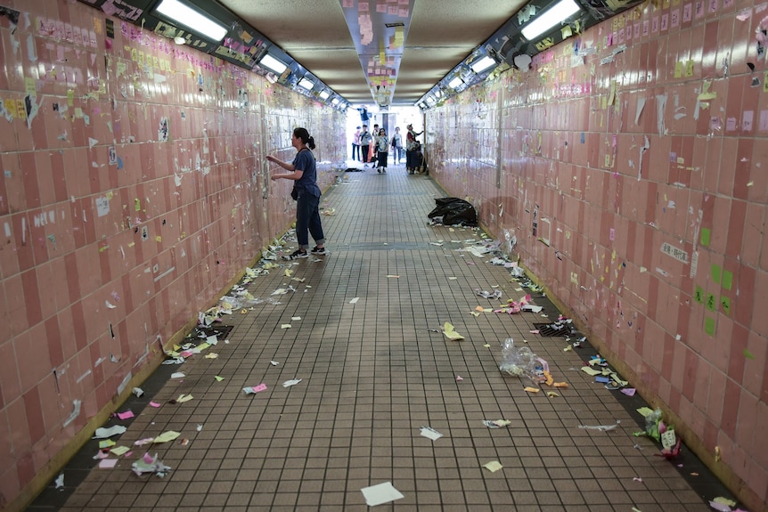 A tunnel with bits of ripped paper all over the ground as a woman cleans post it notes off walls