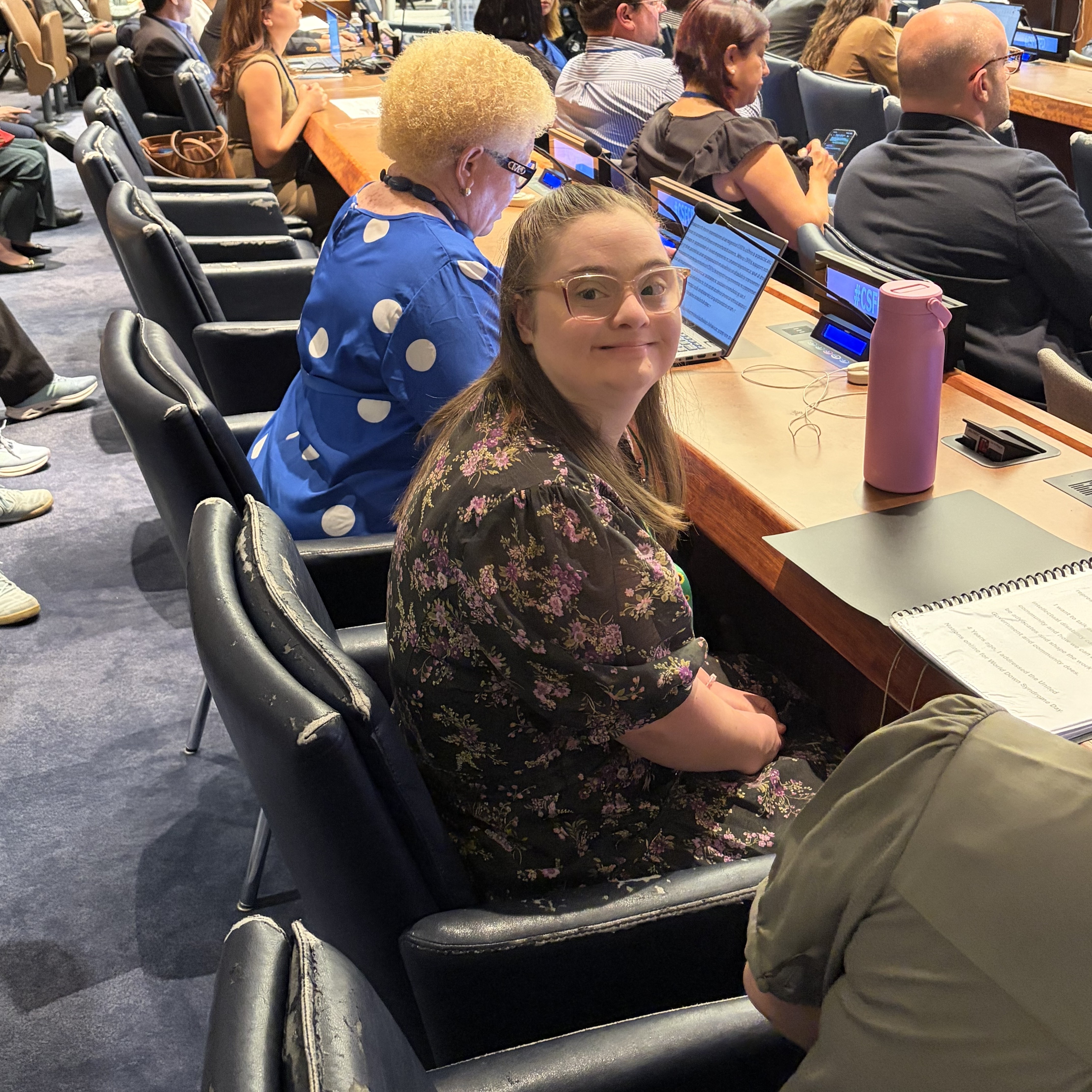 A woman with Down Syndrome sits at the UN and looks at the camera.