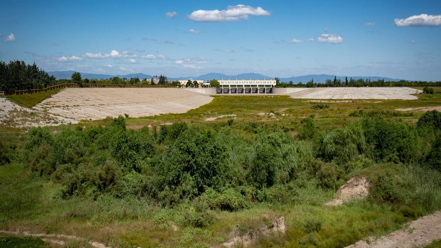 A wide shot of a dry dam wall showing grass and concrete.