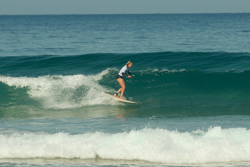Young blonde woman surfing a green wave that is breaking behind her
