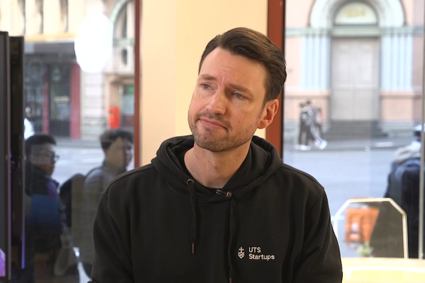 A Caucasian man with brown hair, wearing a black hoodie.