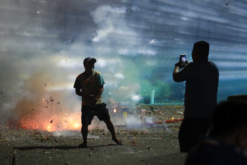 A Filipino poses for a selfie beside exploding firecrackers.