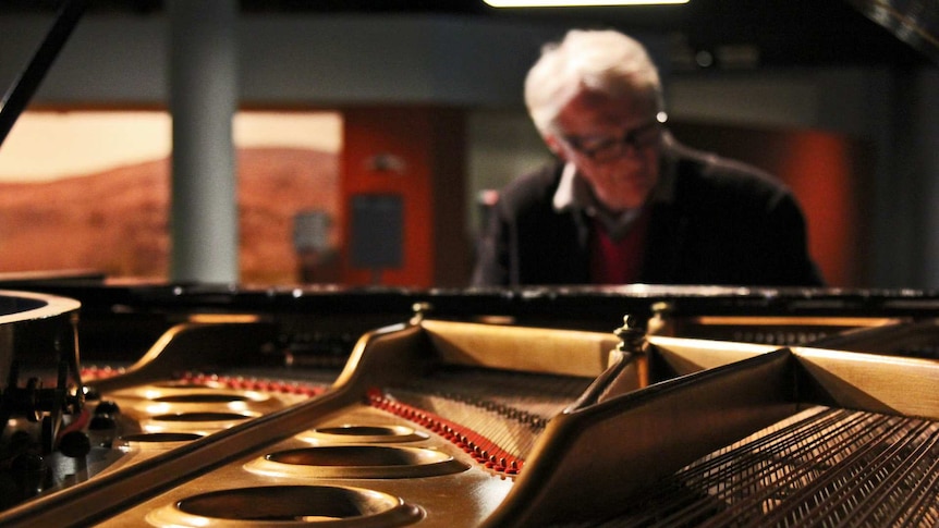 A man plays the piano with the inner workings of the piano on display