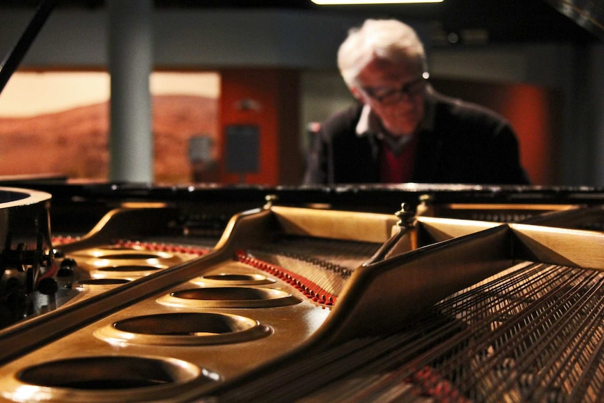 A man plays the piano with the inner workings of the piano on display