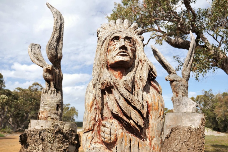 A wood carving of a Native American Indian flanked by two eagles.