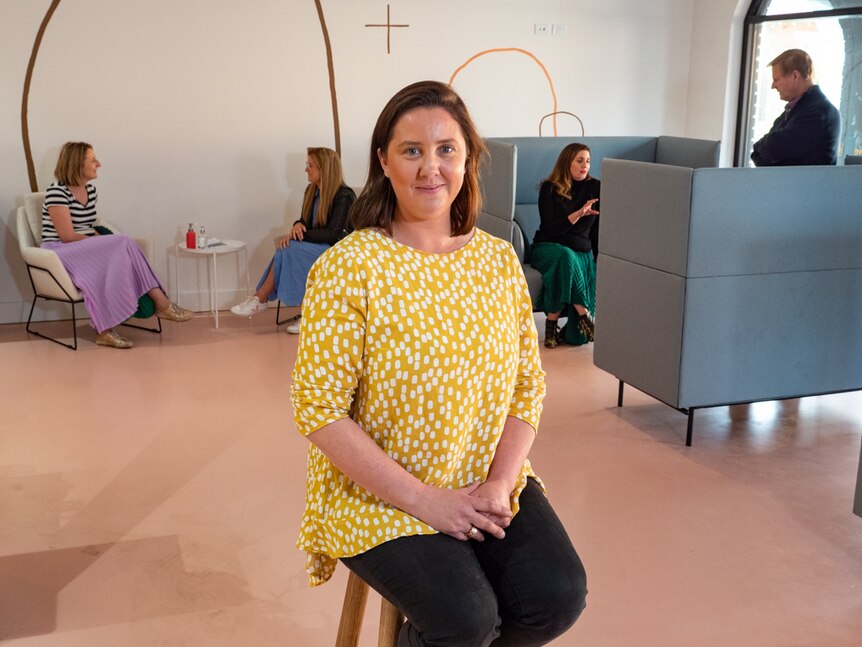 Prue Swain sitting on a chair with four people in the background in a co-working office space.