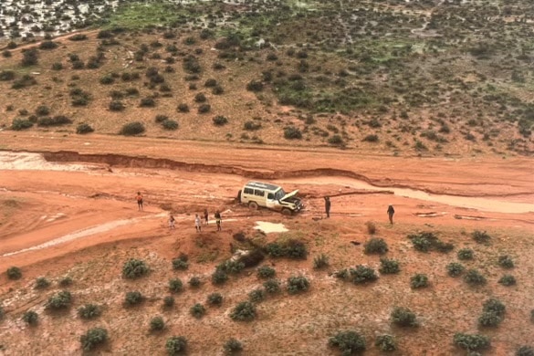 An aerial image of a car and seven people on the side of a flood-damaged outback road.
