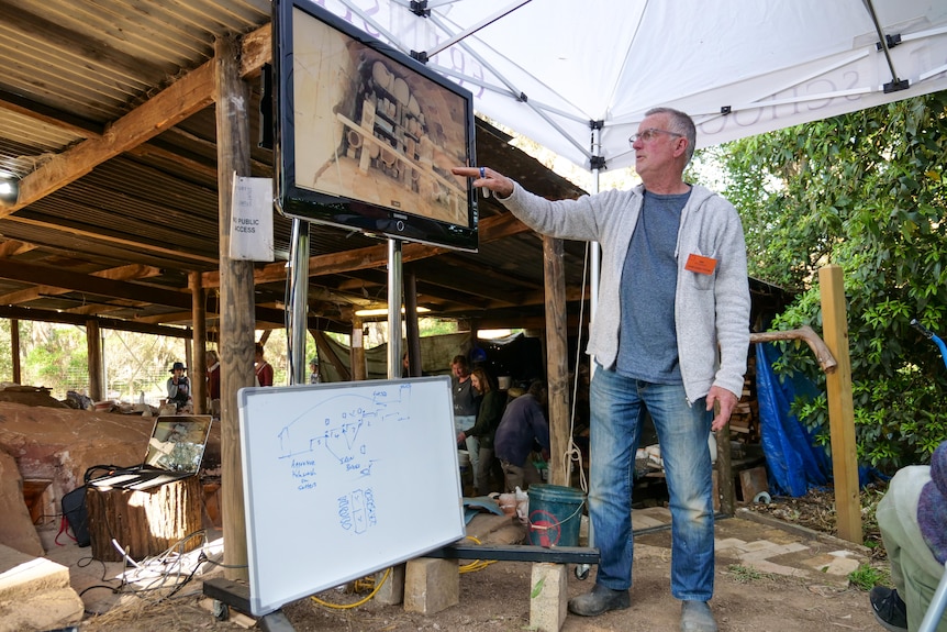 A man points out elements of the kiln packing process to students watching nearby. 