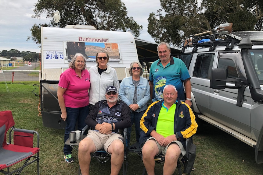 Campers at the Mount Gambier Fairgrounds in front of their trailer, two sitting on chairs, smile at the camera.