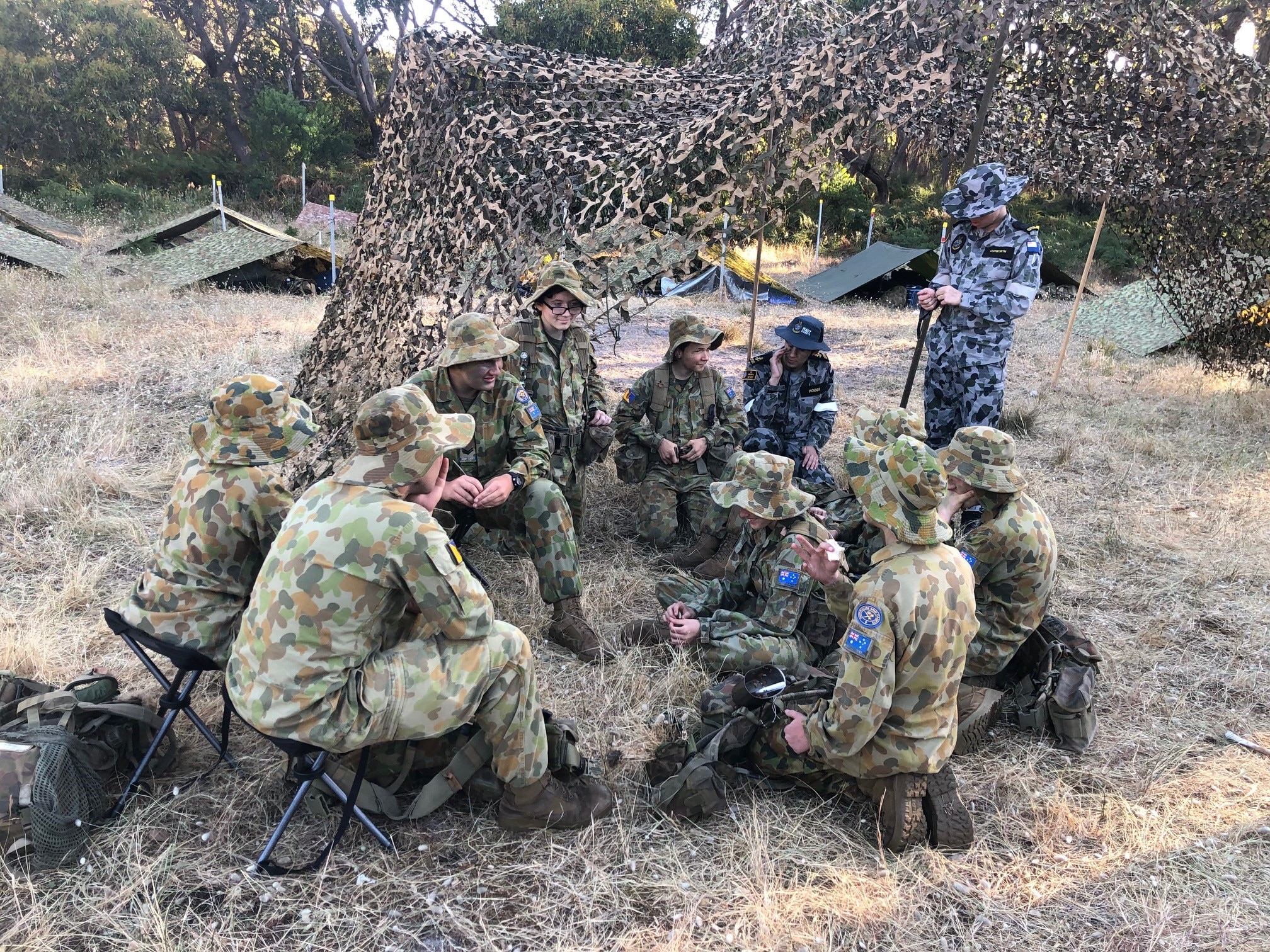 A group of army cadets in uniform sitting around on seats and talking.