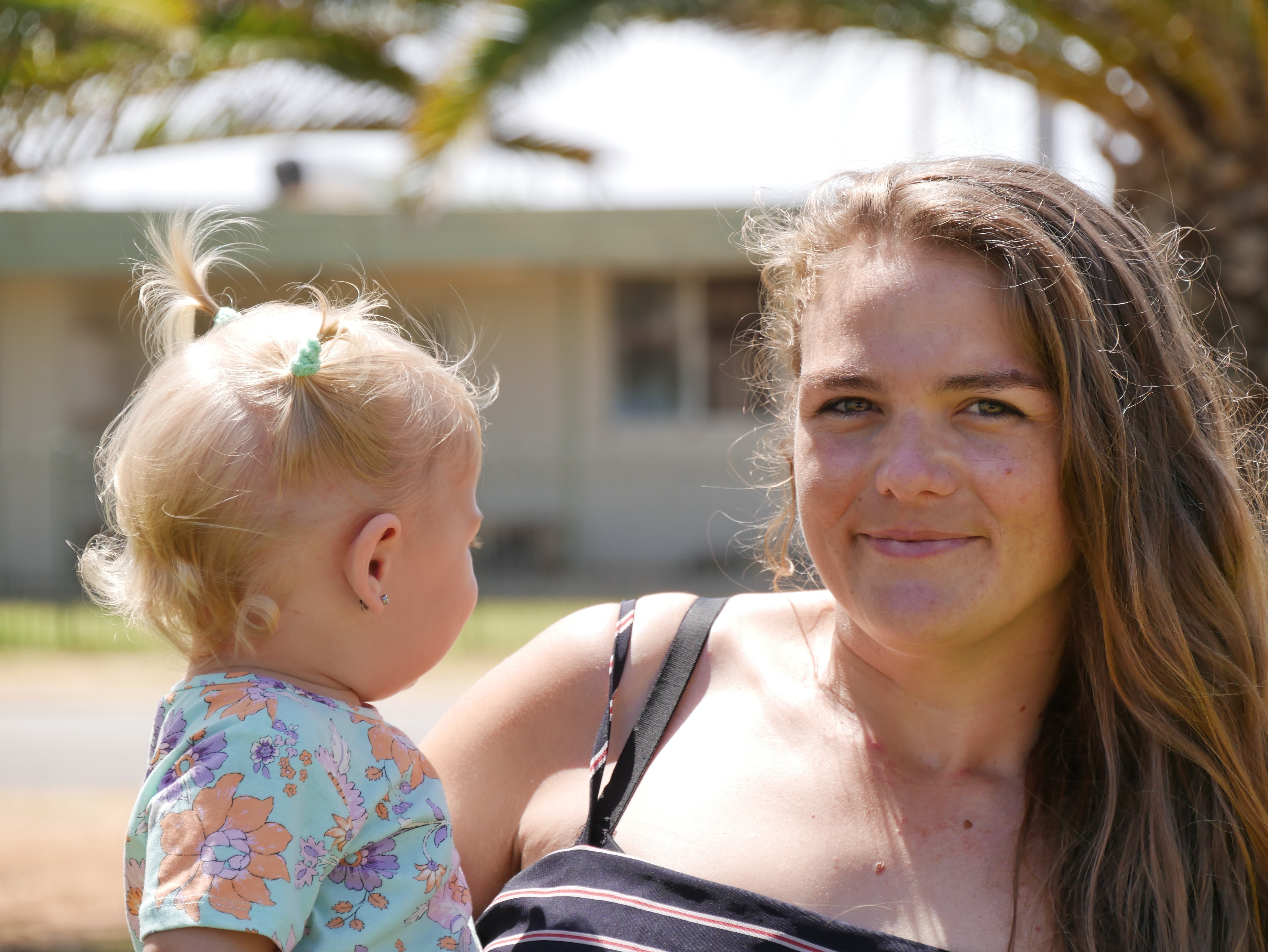 Woman holds baby while staring into the camera. The baby is looking away from the camera. The woman has light brown hair.