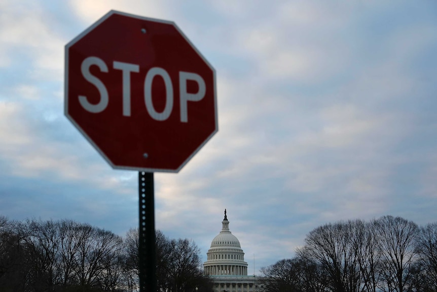 A stop sign with the US Capitol building under grey skies