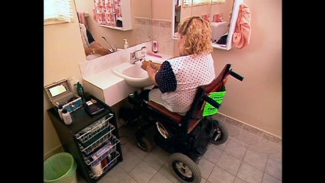 Woman in wheelchair washes hands at bathroom sink