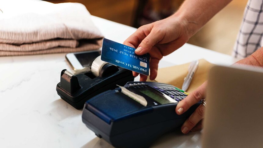Man swiping a credit card in an EFTPOS machine on a shop countertop.
