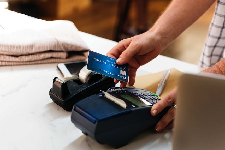 Man swiping a credit card in an EFTPOS machine on a shop countertop for a story about the worth of rewards and credit cards.