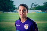 Sam Kerr poses in a Perth Glory uniform in front of a soccer field.