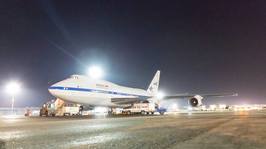 A 747SP airliner, slightly shorter and taller than a normal 747 and with a modified rear section, sits on the tarmac at night.