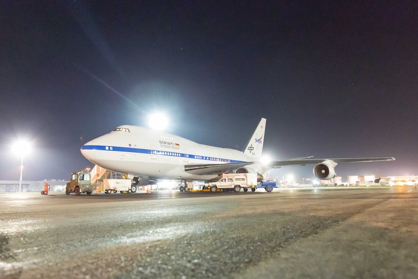 A 747SP airliner, slightly shorter and taller than a normal 747 and with a modified rear section, sits on the tarmac at night.