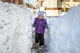 A 3 year old girl walks down a pathway cut in deep snow, which is as tall as her.