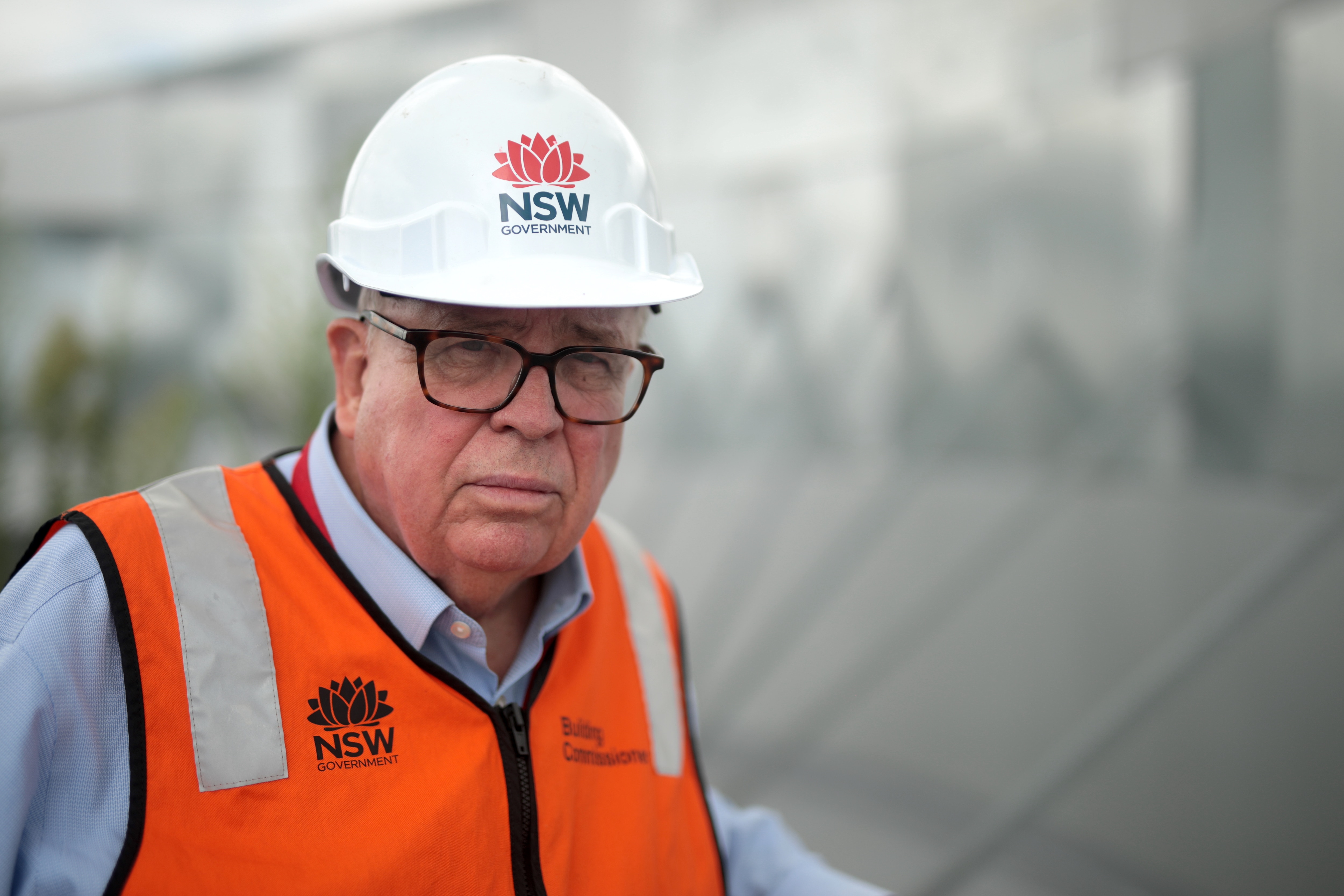 Man wearing a blue business shirt, orange hi-vis and hard hat standing on a roof.