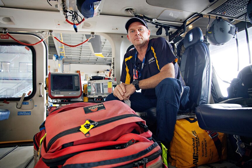 un trabajador de emergencia masculino sentado junto a una bolsa roja en un helicóptero