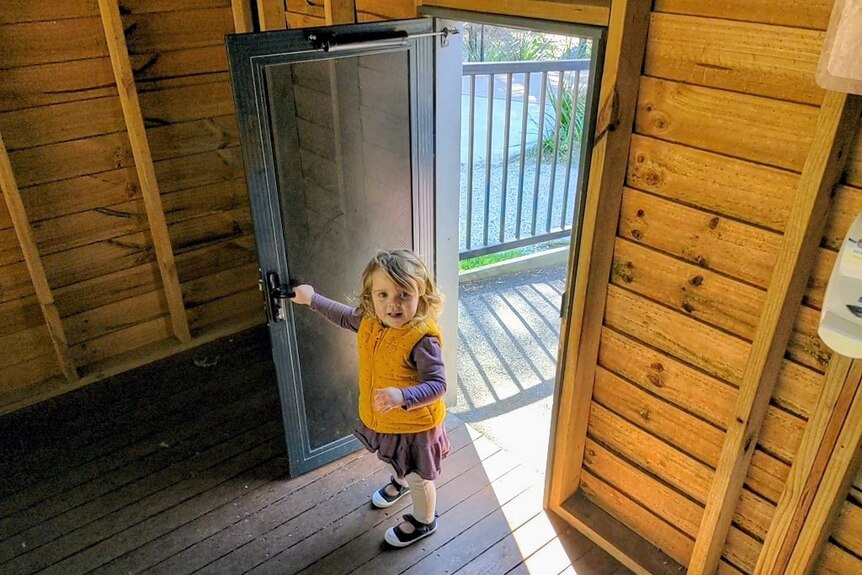 A little girl comes through a small door.