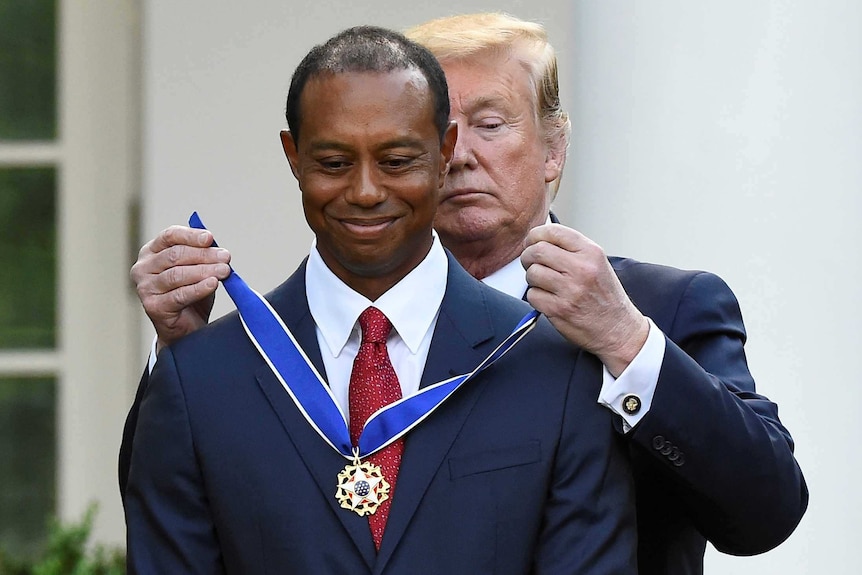 Donald Trump stands behind Tiger Woods as he fastens a medal around his neck