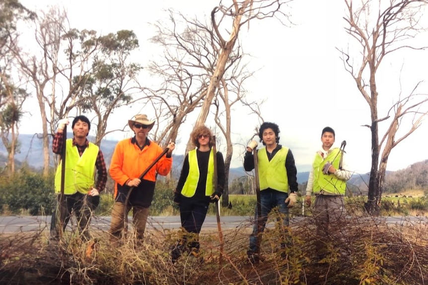 Five volunteers clad in hi-vis stand on the edge of a Victorian roadway.