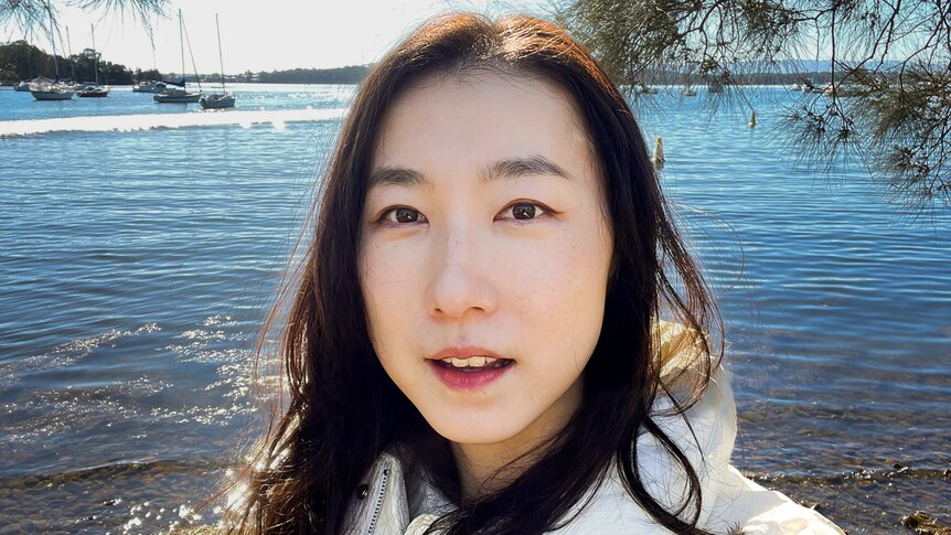 A selfie of a young Asian woman near the water. She is looking directly into the camera.