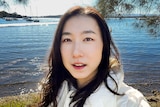 A selfie of a young Asian woman near the water. She is looking directly into the camera.