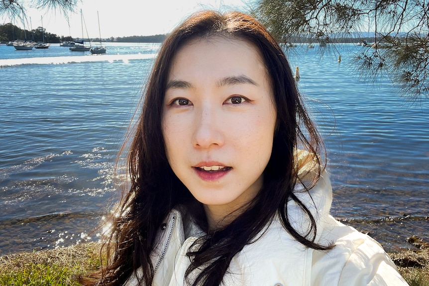 A selfie of a young Asian woman near the water. She is looking directly into the camera.