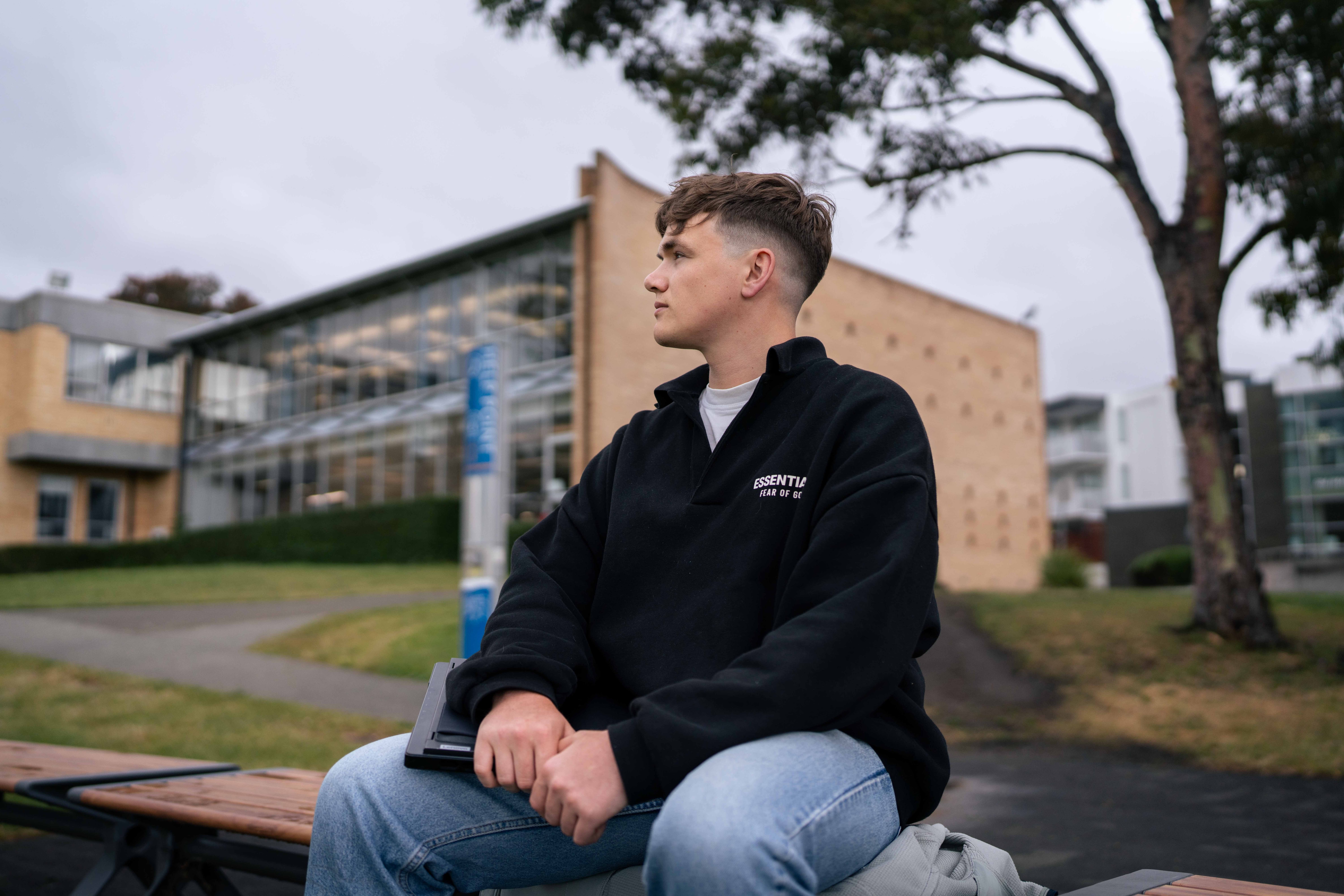 Man sits on park bench looking out to a university in the distance