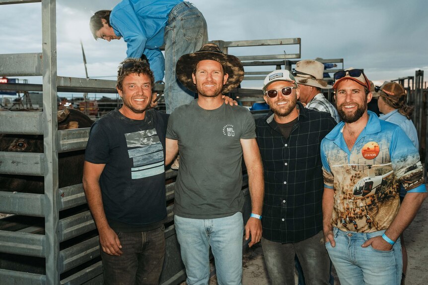 Four men standing next to a cattle chute at an outback  rodeo.  