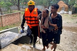 Rescue workers help an elderly woman to reach a makeshift shelter, guiding her up stairs as rain falls in the background.