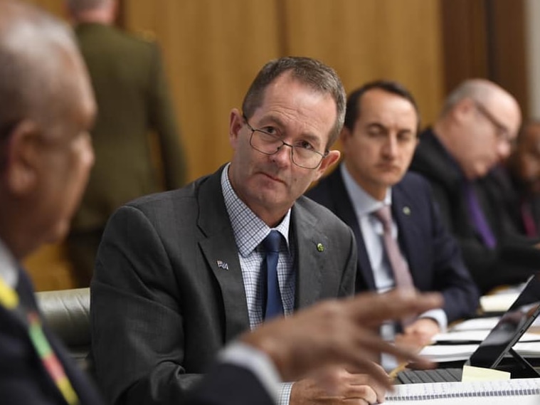 Man in suit speaks to other men in suits at table