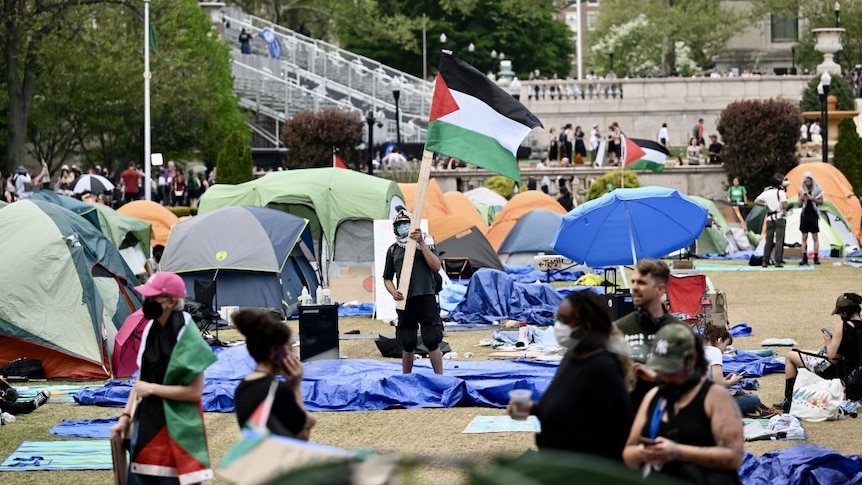 Student holding a Palestinian Flag amongst tents