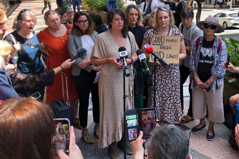A group of people standing together with one women in front of a microphone