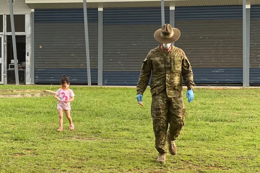 A toddler walks next to a soldier