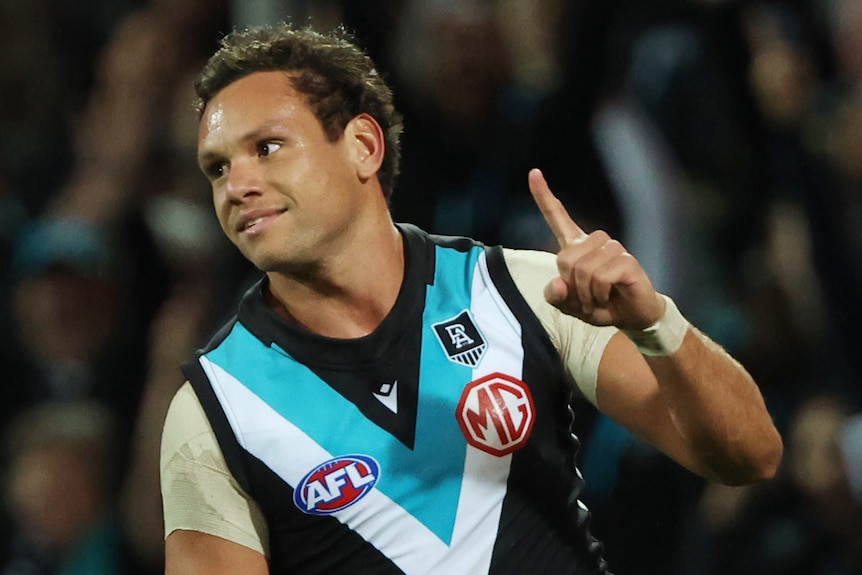 A Port Adelaide AFL player raises a finger on his left hand as he smiles and celebrates a goal against St Kilda.