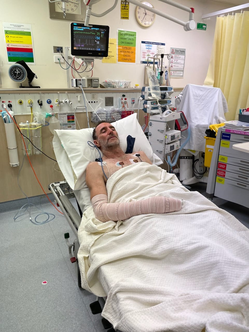 A man in hospital, hooked up to drips, with shut eyes