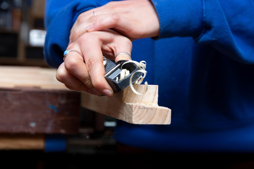 A close up image of a hand sanding wood