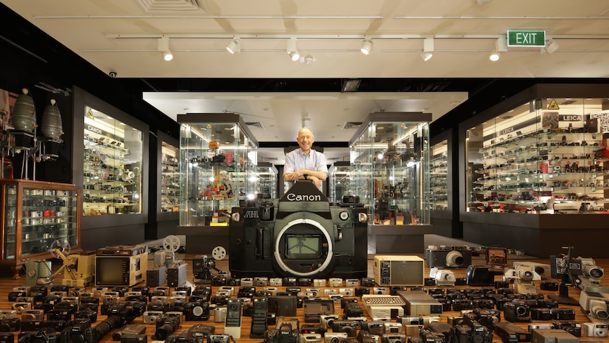 man standing in shop with hundreds of cameras