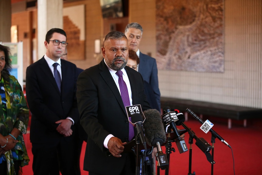 A man in a suit speaks at a lecture while others watch on. 