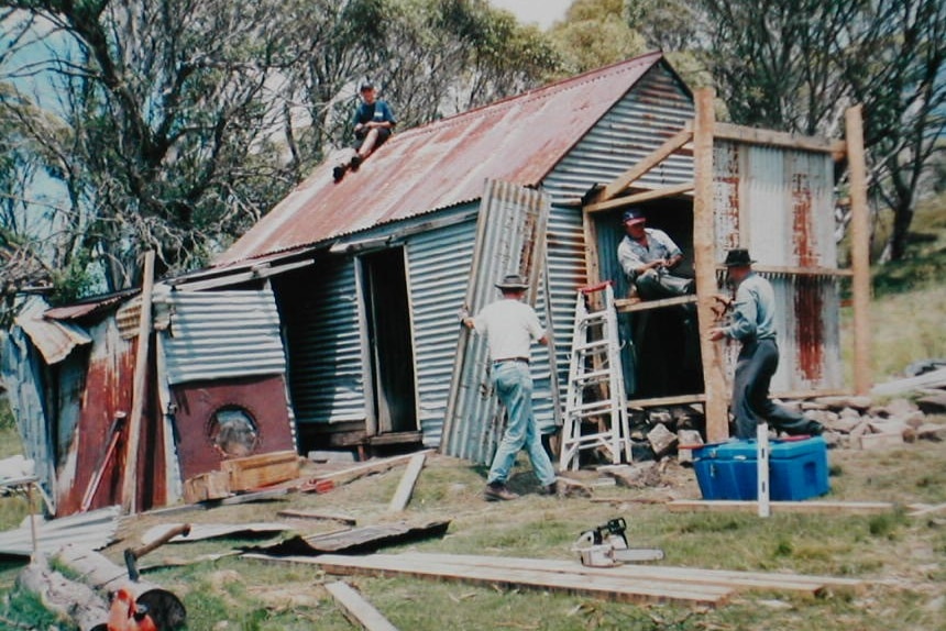 A historic photo of people restoring an old hut.